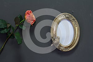 Empty gold vintage oval frame in Victorian style and rose flower on a gray wall, background or concept