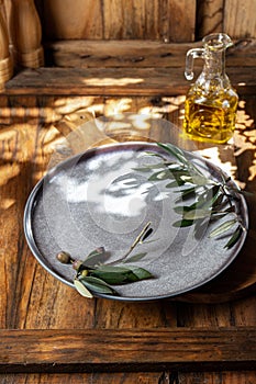 Empty gray plate with olives tree branches. Wooden bacground, Sunlight