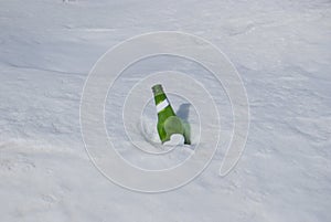 Empty green beer bottle sticks out of the snow