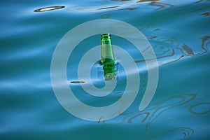 Empty green glass bottle in blue sea water