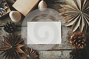 Empty greeting card and christmas paper stars, wooden tree and pine cones on rustic background. Flat lay. Space for text.