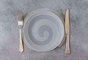 1 empty grey plate, fork, knife on grey concrete background, top view