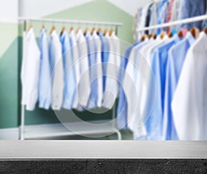 Empty stone surface and clean clothes on hangers in dry-cleaning, space for text