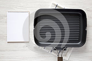Empty grill pan, blank notepad on a white wooden background, top view. Overhead, from above, flat lay. Copy space