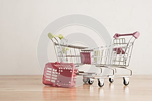 Empty grocery cart or supermarket trolley and basket on wooden with white wall background copy space. Food shortage, food crisis