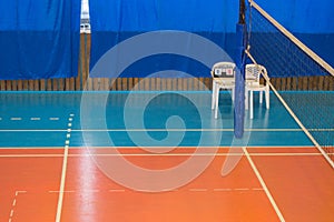 An empty gym with a volleyball net, chairs and display Board in the school