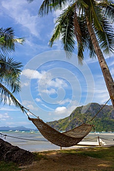 Empty hammock with palm tree and boat on tropical beach. Philippines resort landscape. Idyllic vacation concept.