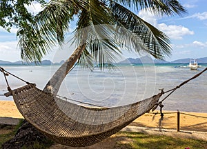 Empty hammock with palm tree and boat on tropical beach. Philippines resort landscape. Idyllic vacation concept.