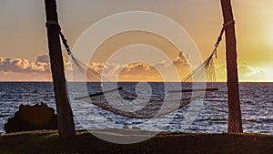 Empty hammock between two palm trees against scenic sunset over Pacific ocean.