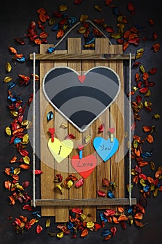 Empty heart blackboard on wood. Valentine\'s day concept. Dark background with colorful dry rose petals.