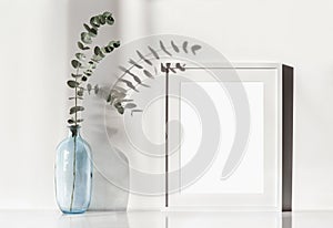 Empty horizontal frame mockup in modern minimalist interior with plant in trendy vase on white wall background.
