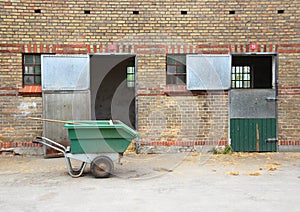 Empty horse stables with dirt wagon on asphalt