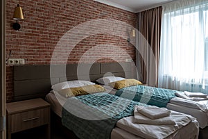 Empty hotel room with beds near red brick wall and window