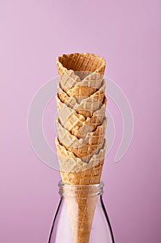 Empty ice cream cones in glass milk bottle against purple background