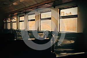 The empty interior of an electric train car, illuminated by rays of sunlight streaming in through the windows during sunset. A