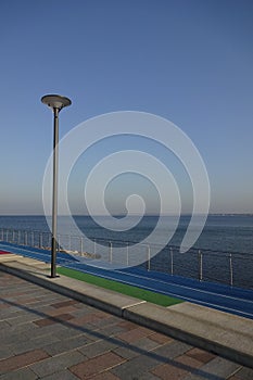 Empty jogging running lanes with white lines, blue artificial textured ground. Lamppost and handrails by the side