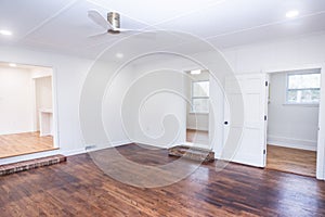 An empty living room or den area with built in cabinets and bookcases, windows and a fan with a step up