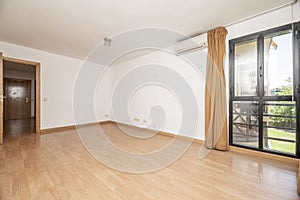Empty living room of a house with a light brown laminate floor, a bay window with black anodized aluminum windows and light brown
