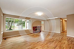 Empty living room interior with brick fireplace and hardwood floor.