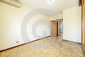 Empty living room with oak parquet flooring and air conditioner on the wall