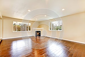 Empty living room with polished hardwood floor and corner fireplace.