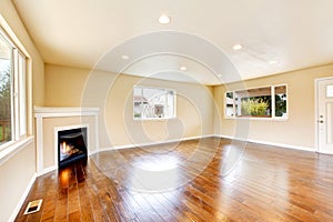 Empty living room with polished hardwood floor and corner fireplace.