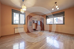 Empty living room with a small bookcase in the corner above shiny hardwood floors and anodized aluminum windows on several walls