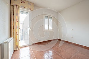 Empty living room with two aluminum windows with triple glazing, red stoneware floors and electric heat accumulator and exit to