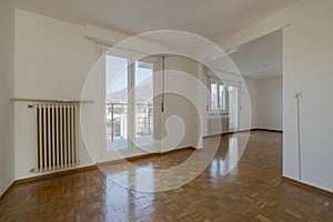 Empty living room with two big and bright windows, where you can see the blue sky and the mountains. On the white walls are two