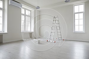 Empty living room with white freshly painted walls, step ladder, and a bucket of paint