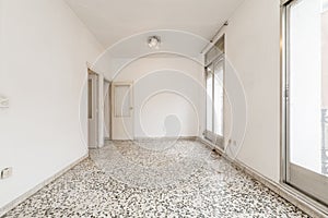 Empty living room with white terrazzo floor with black dots, white walls, wooden access doors and aluminum and glass sliding doors