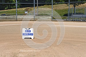 Empty local baseball field on a sunny day, view of pitcherâ€™s mound, home plate and bleachers, Field Reserved sign