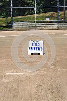Empty local baseball field on a sunny day, view of pitcherâ€™s mound and home plate, Field Reserved sign