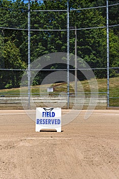 Empty local baseball field on a sunny day, view of pitcherâ€™s mound and home plate, Field Reserved sign