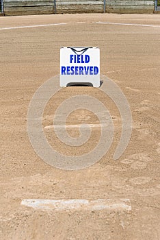 Empty local baseball field on a sunny day, view of pitcherâ€™s mound and home plate, Field Reserved sign