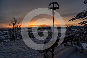 Empty lonely bench and cross with Jesus Christ in cold snowy winter morning in village Martincek, Slovakia