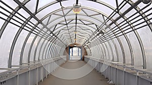 Empty long glass tunnel on the pedestrian bridge, The camera moves through glass tunnel on sunny day with blue sky, at
