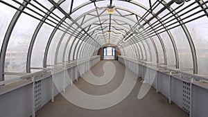 Empty long glass tunnel on the pedestrian bridge, the camera moves through glass tunnel on sunny day with blue sky, at