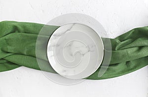 Empty marble plate with green napkin on white textured background.