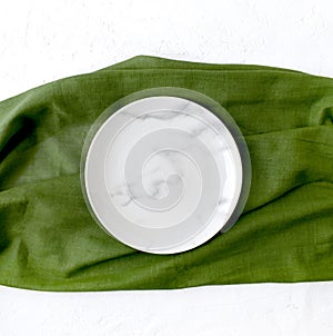 Empty marble plate with green napkin on white textured background.