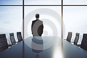 Empty meeting room with big conference table, chairs around and businessman back looking through big window