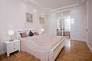 Empty minimalistic interior background, bedroom of modern apartment with big mirrors, double bed, lights on