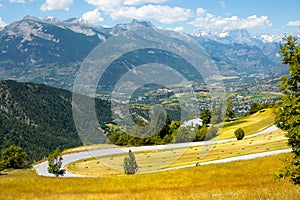 Empty mountain road runs past the beautiful yellow meadows in the French Alps.