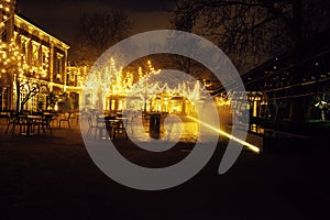 Empty night restaurant, lot of tables and chairs with noone, magic fairy lights on trees like christmas