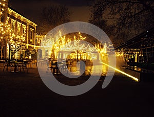 Empty night restaurant, lot of tables and chairs with noone, magic fairy lights on trees like christmas, luxury