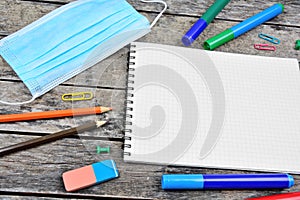 Empty notebook with face mask and many school tools