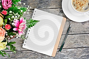 Empty notebook with pen, coffee cup and colorful flowers on table