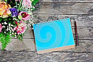 Empty notebook with pen and flowers on an old wooden table