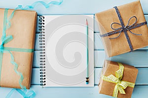 Empty notebook, pencil and gift or present box packed in kraft paper on blue wooden table