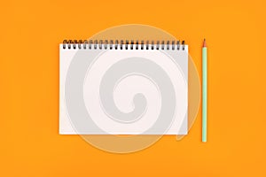 Empty notebook and pencil on orange background, top view.